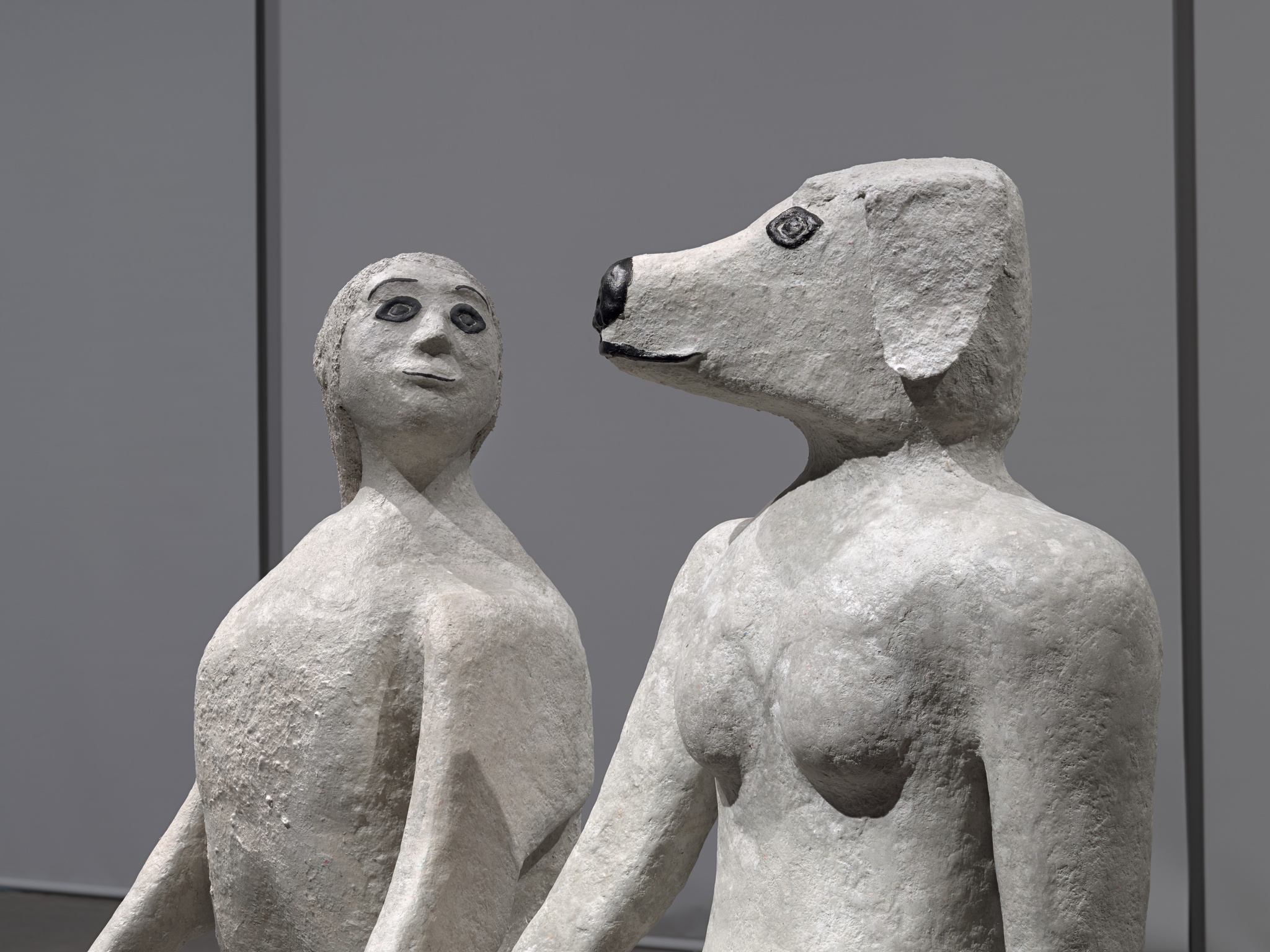 Two sculptures of anthropomorphic figures seen from the shoulders up. One has the head of a woman and the other the head of a dog.