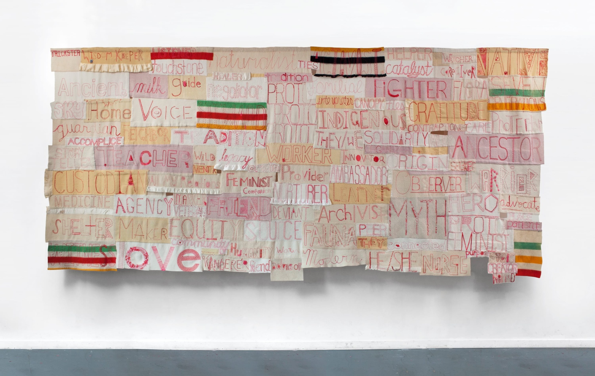 Cream, tan, and pink squares of fabric overlapping each other in a rectangle shape with words like "love," "voice," and "ancestor" embroidered in red. 
