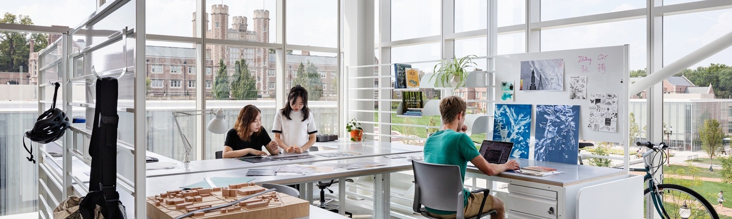 Students working together at desks in a studio facing out towards Brookings Hall.