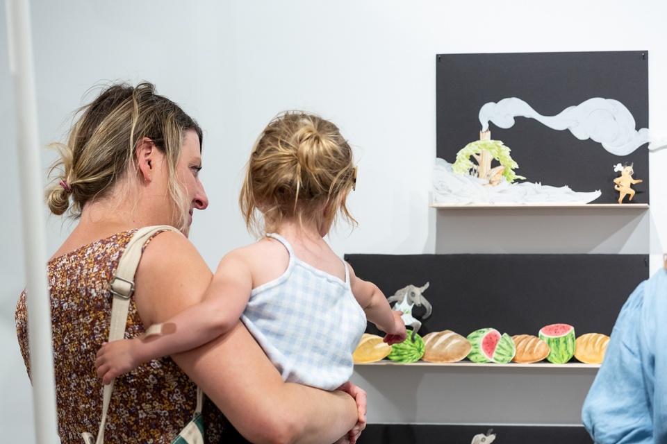 A small child points at an illustration on the wall of a wolf on a watermelon