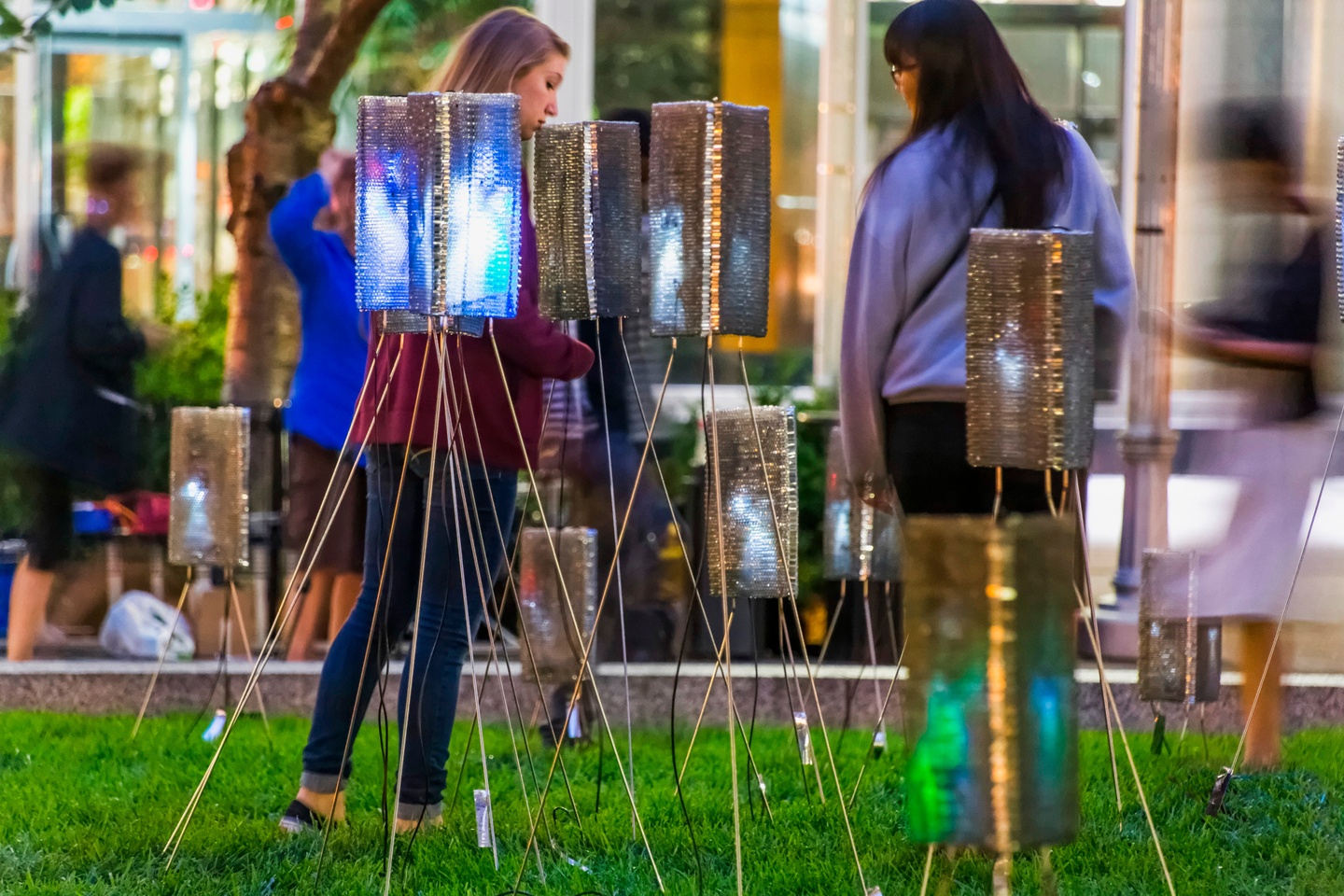 people walking on the grass among an art installation of soft lights on stands