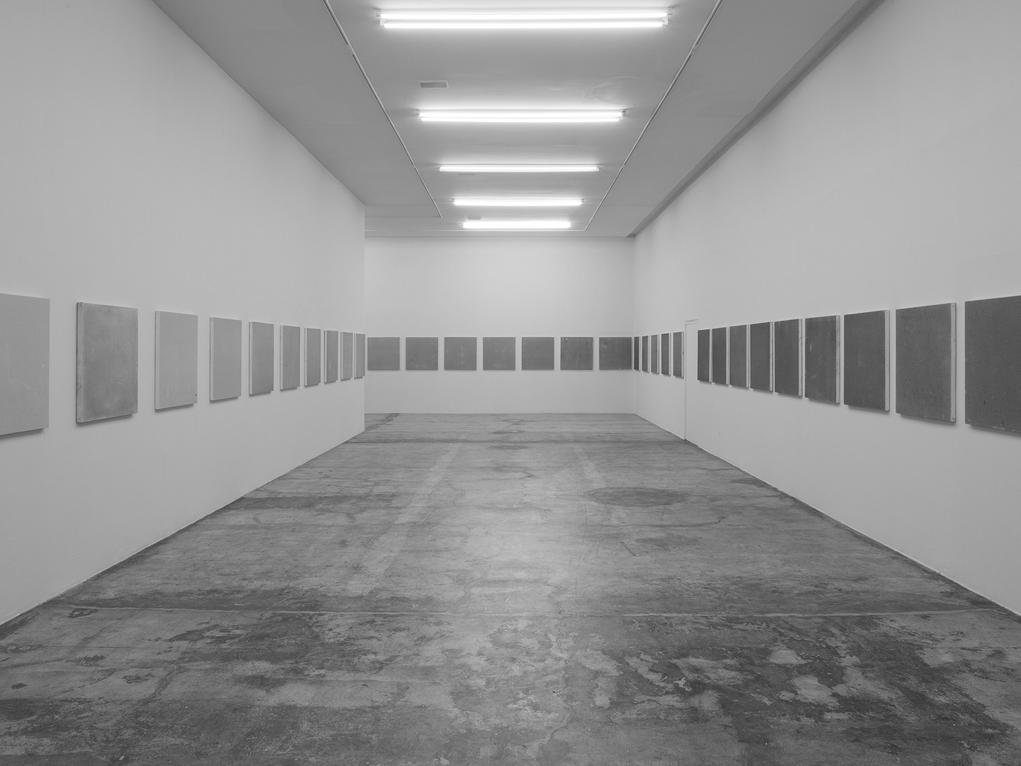 A sequence of square, gray canvases that progressively turn darker as installed in a line around a gallery