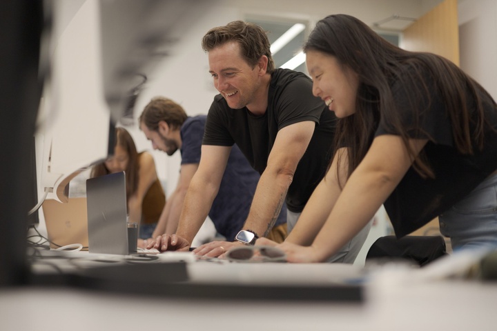 Two people standing at computer with two others in the background