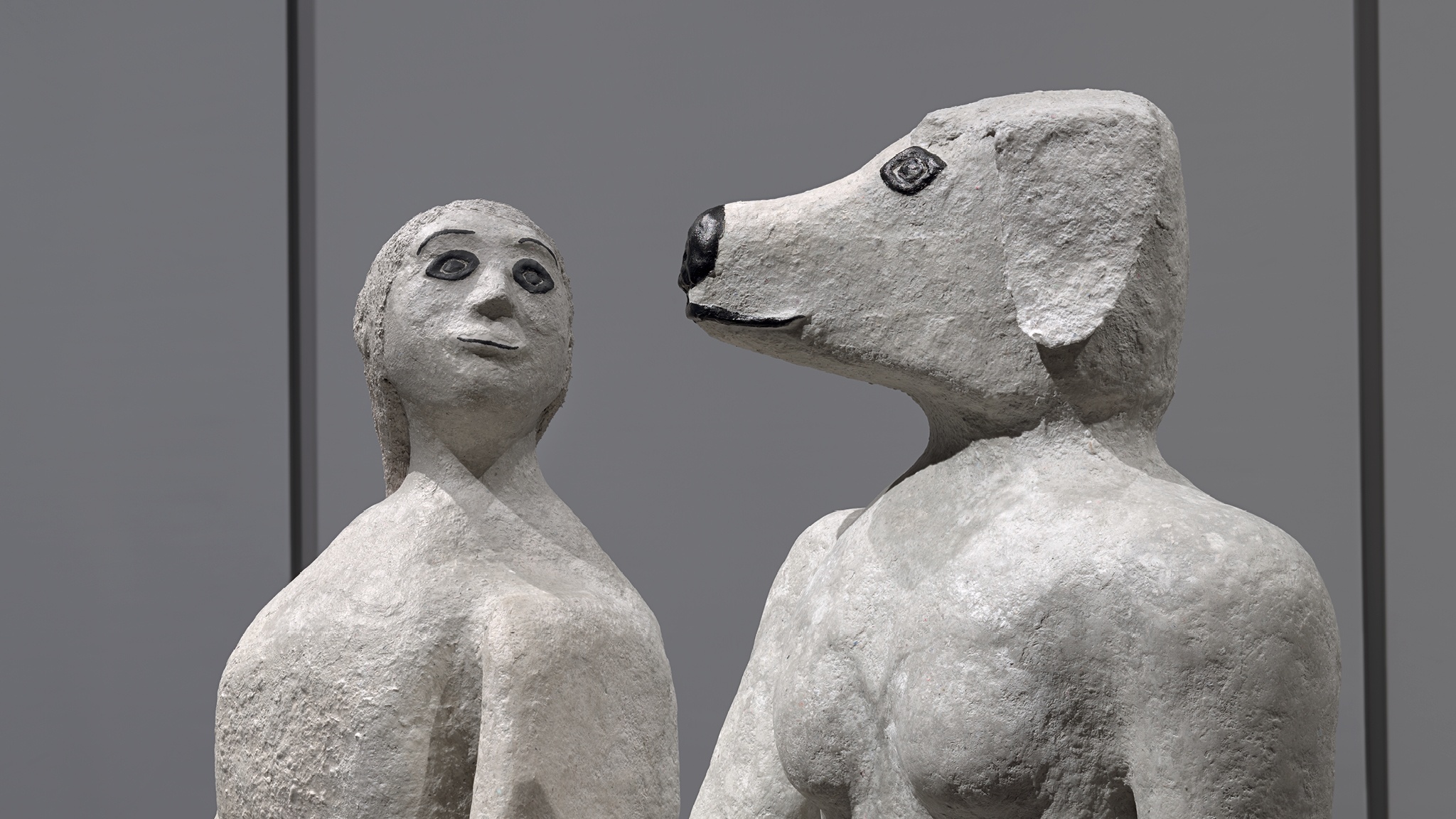 Two sculptures of anthropomorphic figures seen from the shoulders up. One has the head of a woman and the other the head of a dog. 