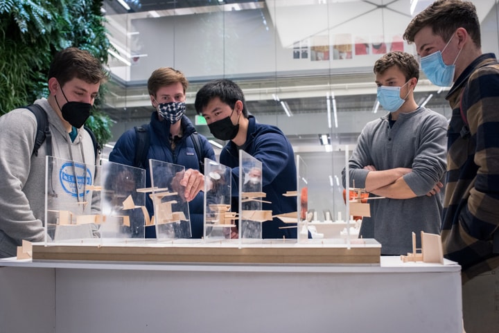 Four people watch as a fifth demonstrates removing a plexiglass plate with balsa wood models stuck to it from an arrangement of seven other similar plates.