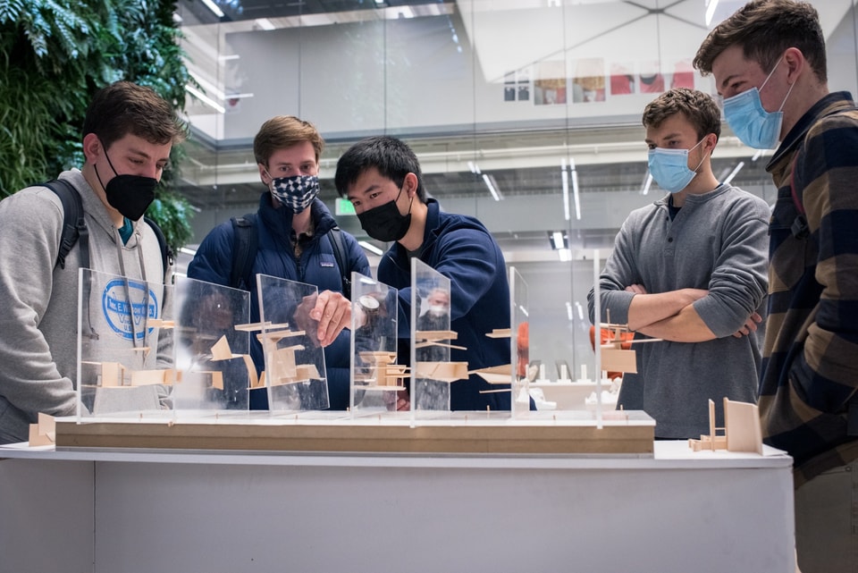 Four people watch as a fifth demonstrates removing a plexiglass plate with balsa wood models stuck to it from an arrangement of seven other similar plates.