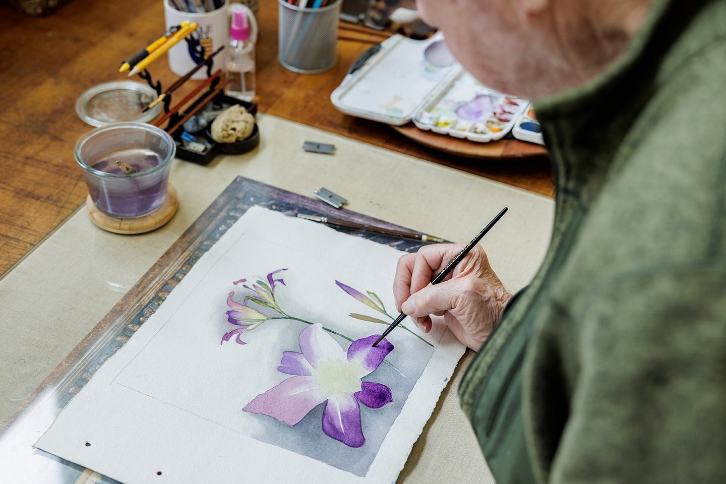 close up of Moore's hand as he paints a purple flower