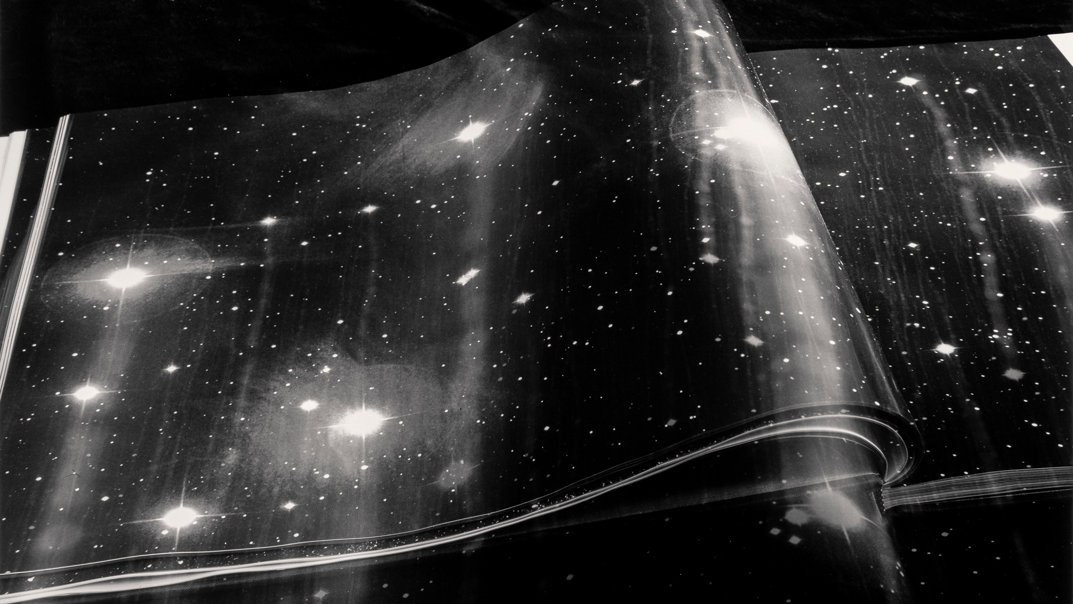 A black and white photograph with sparkling stars and an open book with galaxy printed pages.