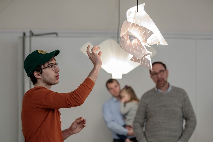 Person gestures at a hanging white asymmetrical lamp and speaks.