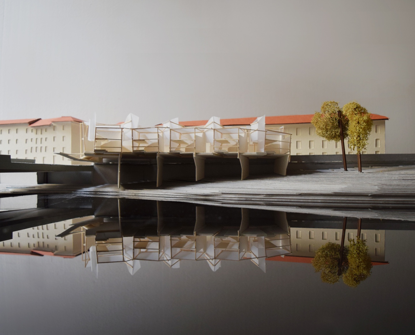 Scale model of a pier structure on a waterfront, backed by hotel buildings with red roofs.