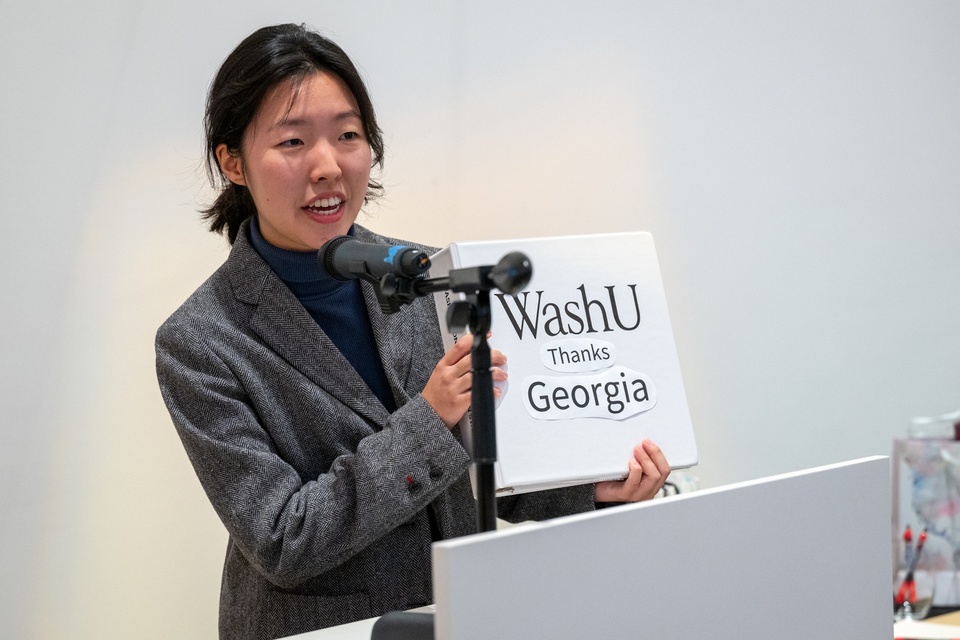 Student at lecturn holds up a binder labeled "WashU Loves Georgia."