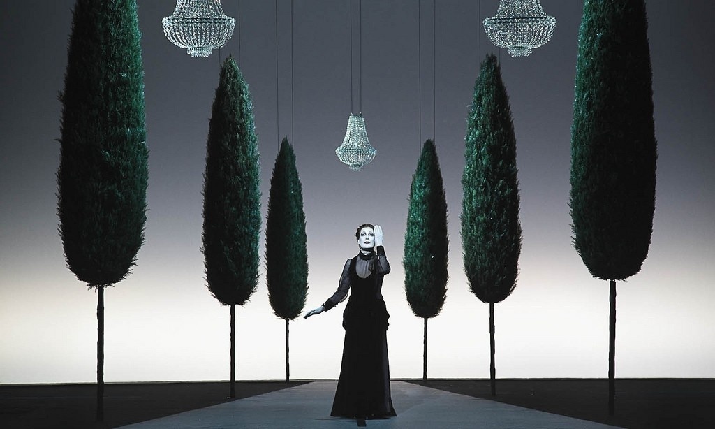 Woman standing on path flanked by trees with three chandeliers
