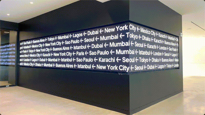 View of high-resolution screen wrapping around corner playing white text of city names on black background on black wall