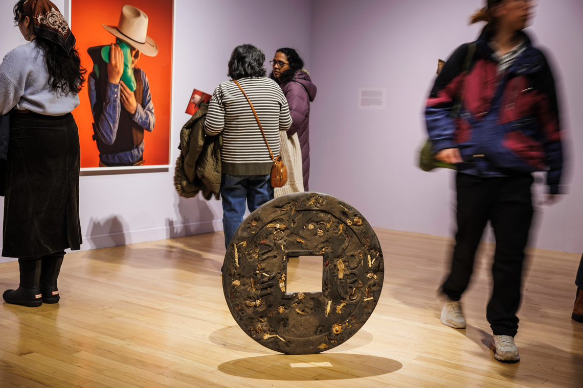 enlarged chinese coin sculpture lit casts shadows as people move around a gallery space