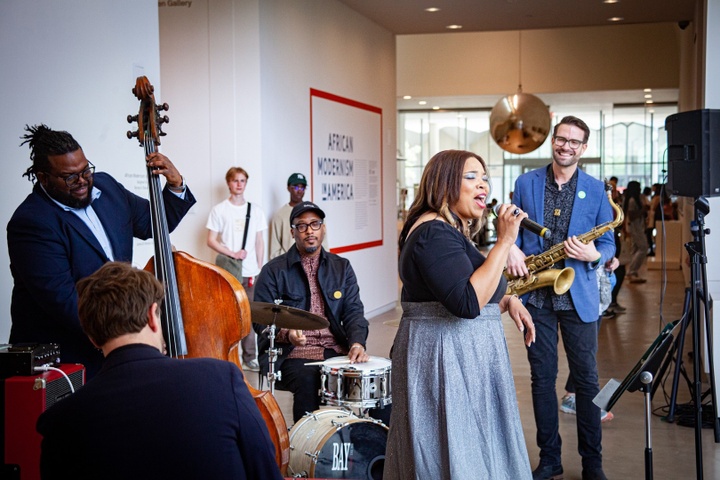 Jazz quartet performs with a singer in the foyer of the Kemper Art Museum outside the entrance of an exhibit labeled "African Modernism in America."