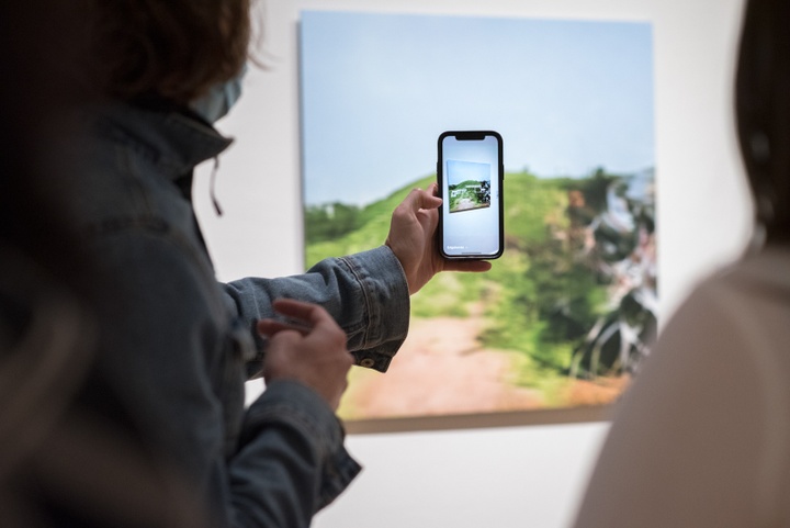 Over the shoulder view of a person holding a phone camera up to a digital print on the wall.
