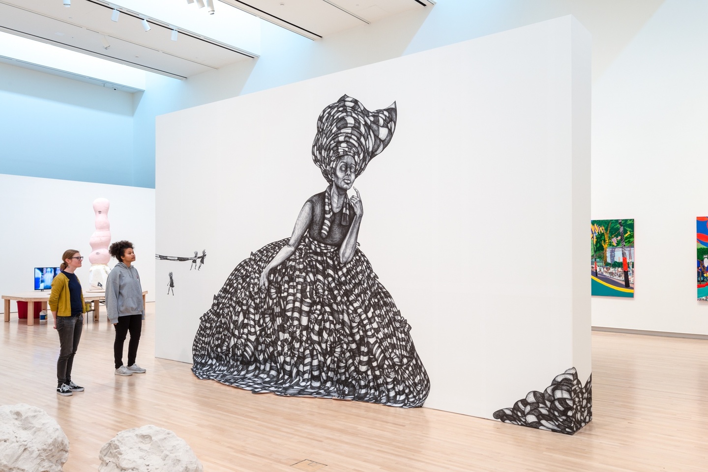 Gallery view of the installation Source of All Hair, Wearer of All Socks. A ballpoint pen drawing of a lady with a wrap headdress made of striped material and a large poofy dress of the same striped material