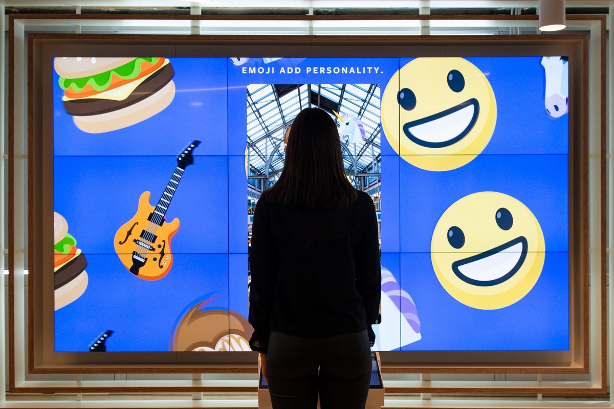 Silhouette of young woman standing in front of large framed screen that displays a cascade of emojis