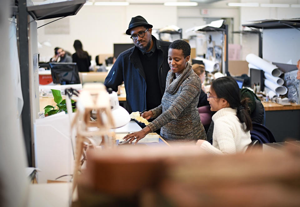 Visiting faculty Andres L. Hernandez and Amanda Williams visit a student in studio, discussing her work at her desk.