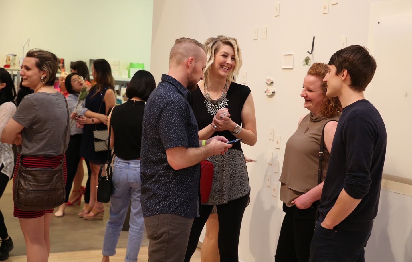 A group of people interacting in a gallery space filled with other people