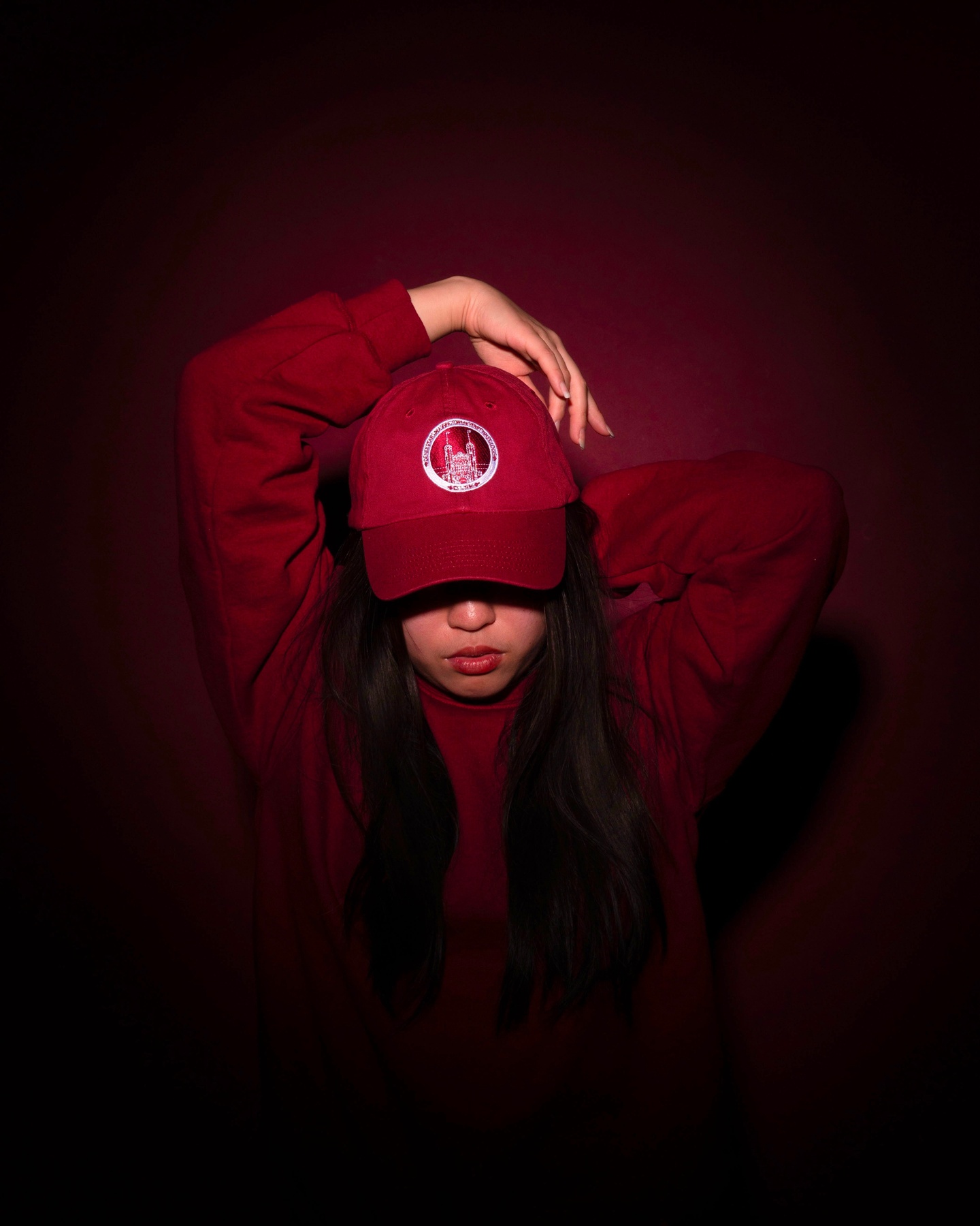 A person with a maroon sweatshirt and baseball cap lit on a maroon background.