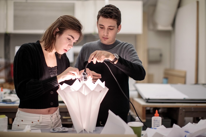 Two students work on assembling a lighted lamp with a frilled top.