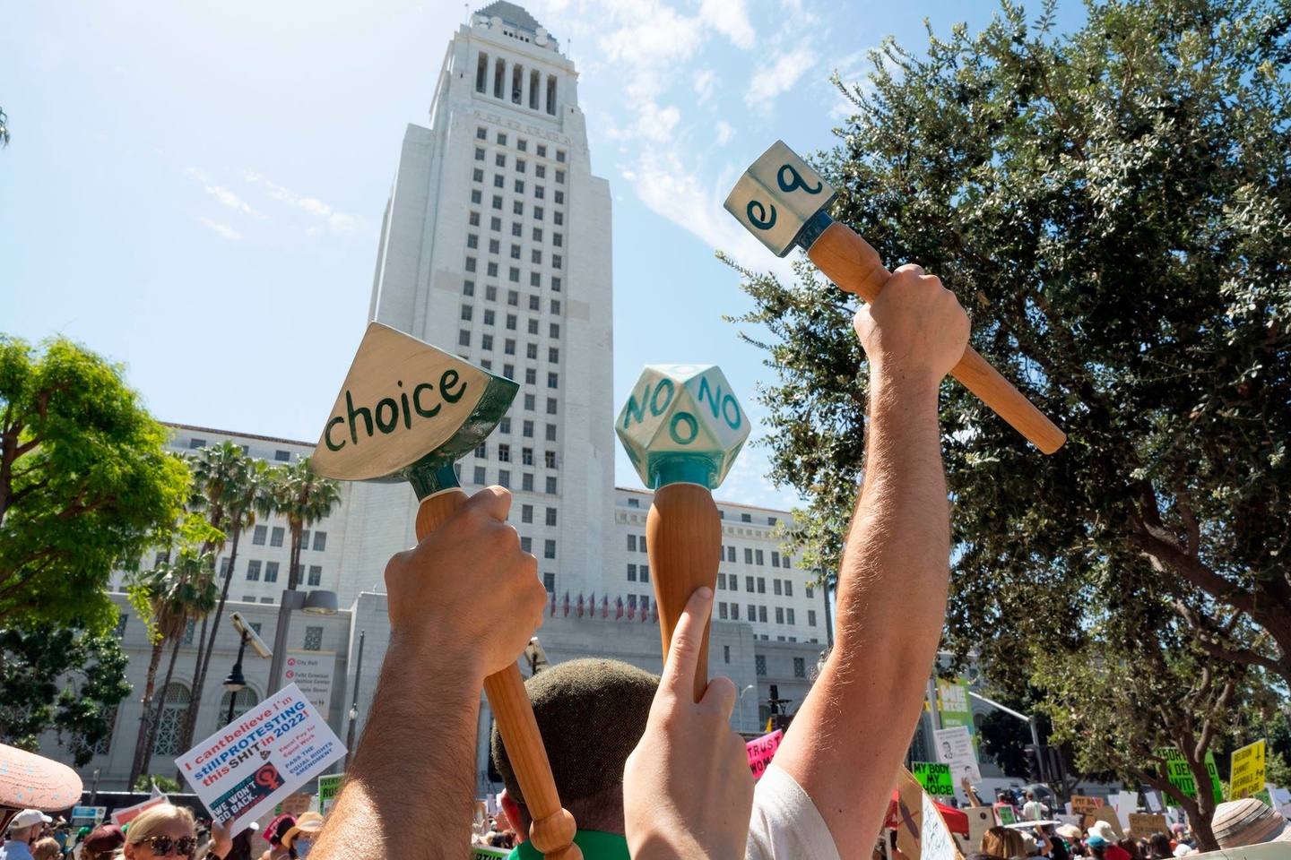 A scene from a protest showing fists, raised in the air, shaking "protest rattles," upon which are printed words like "Choice" and No."