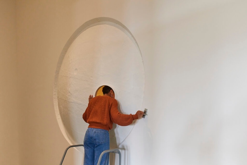 A person peers into a hole in the wall