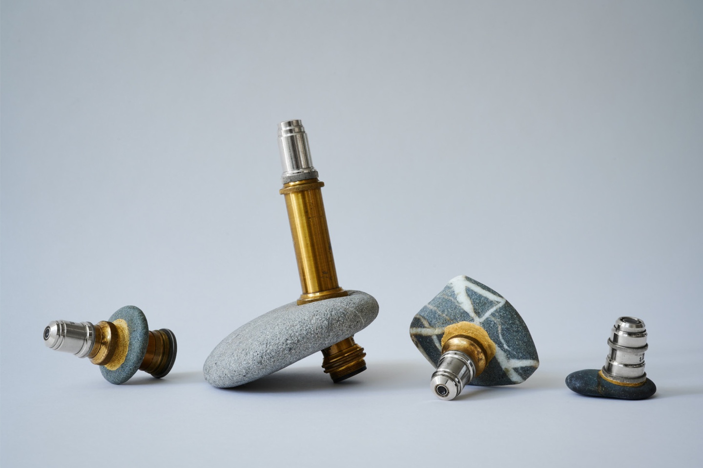 Set of four naturally holed gray hag stones surrounding small silver-and-gold objects.