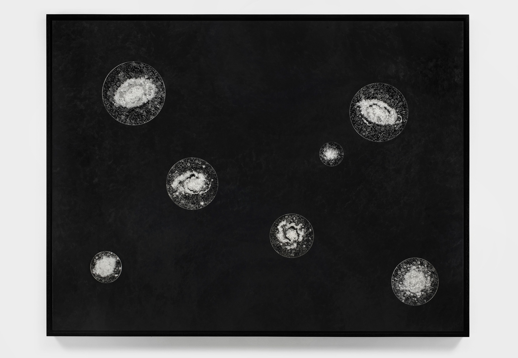 Against a black background are seven circles of various sizes containing clusters of white dots reminiscent of miniature galaxies.