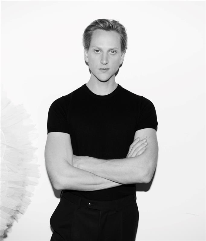 The dancer David Hallberg standing with arms crossed in a black tshirt and pants against a white background