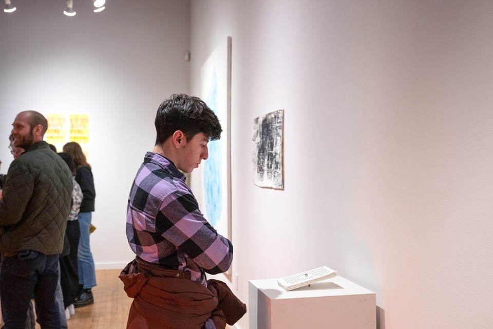 Person looks at a tablet-sized print work on a plinth in a gallery.