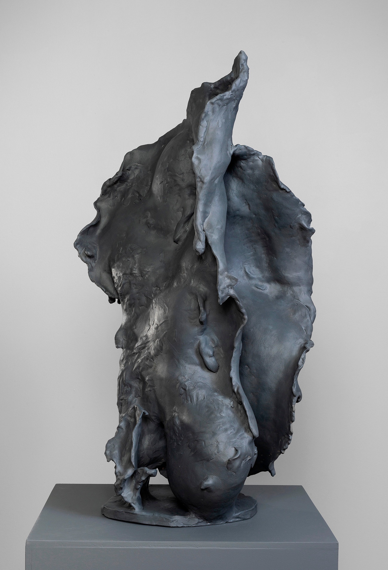 A dark, vaguely amorphous sculpture on a dark gray platform.
