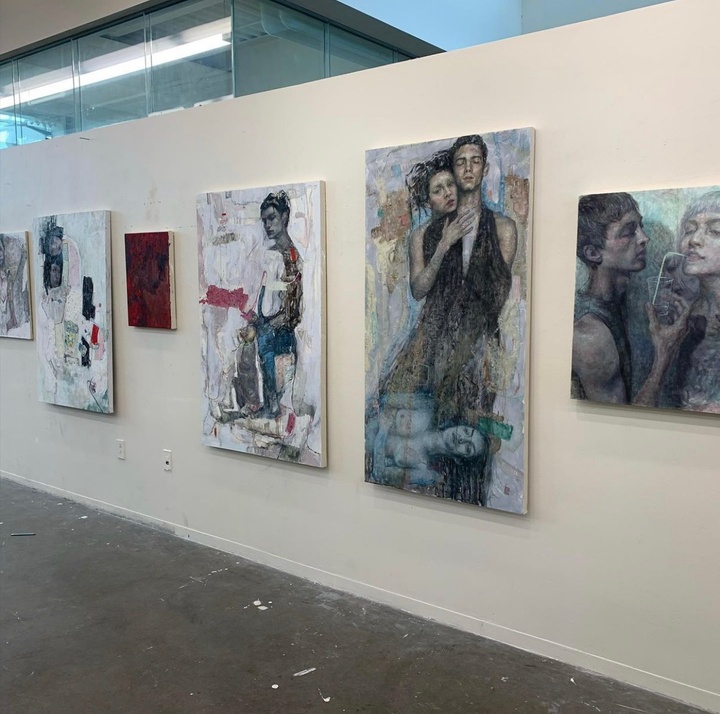 Panels of abstract figure paintings on a white wall. The painting on the far right depicts a person holding up a drink and straw for another person. Another painting depicts a girl hugging a guy from behind while another blue-ish hue girl lays on the ground in the foreground  