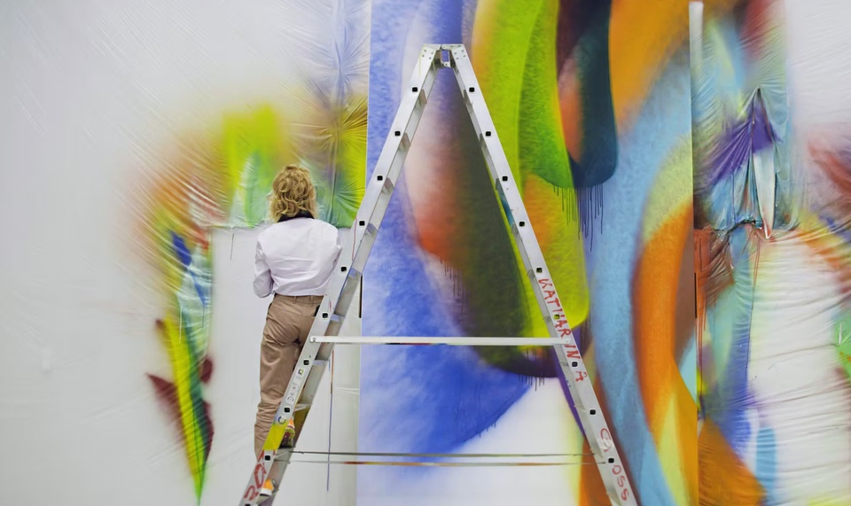 The back of a person standing on a ladder with an abstract painting in the background