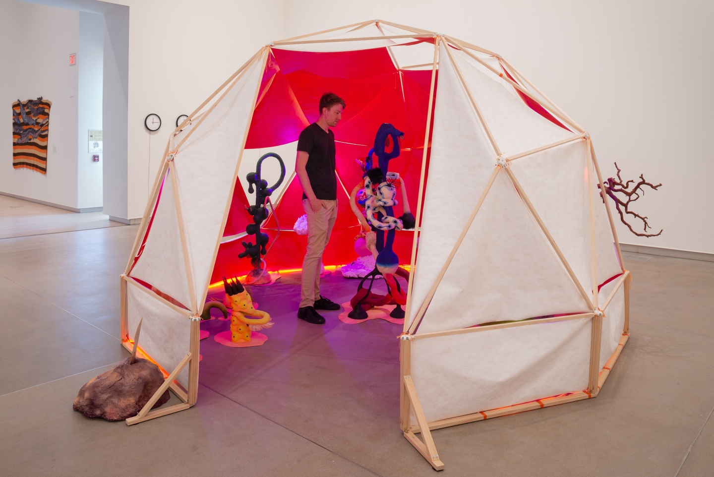 Outside view of a dome-shaped tent. The insides of the bright pink tent with its multiple sculptures is visible