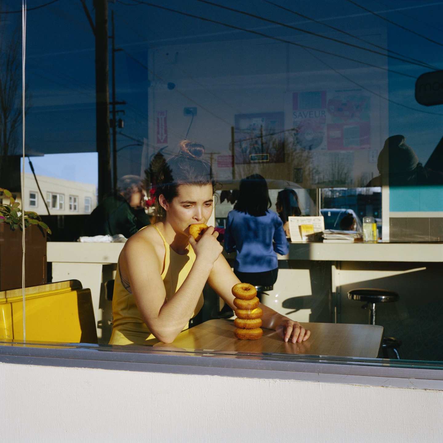 A seated woman eating in the window of a diner with a stack of donuts in front of her