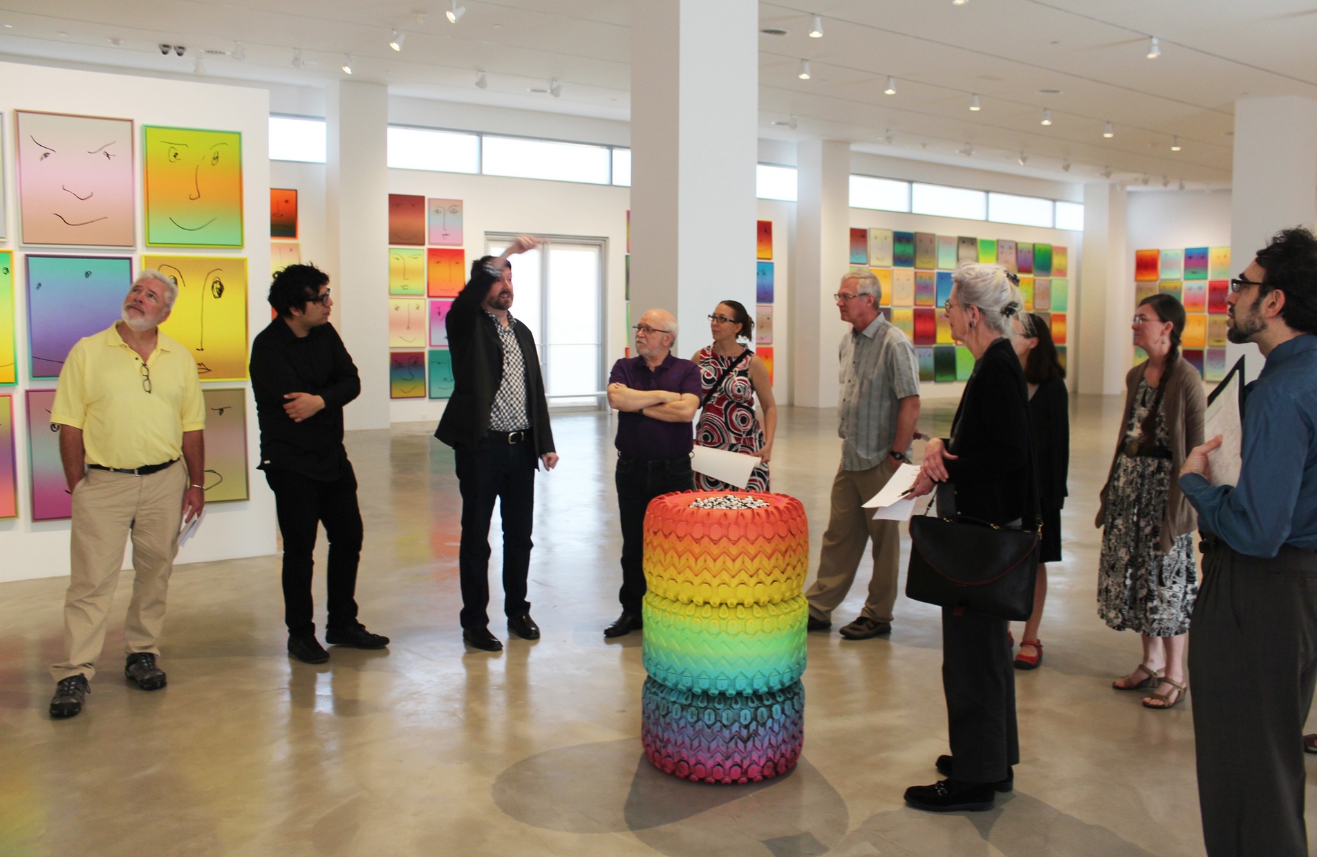 A group of people stand surrounding a sculpture and appear to be talking.