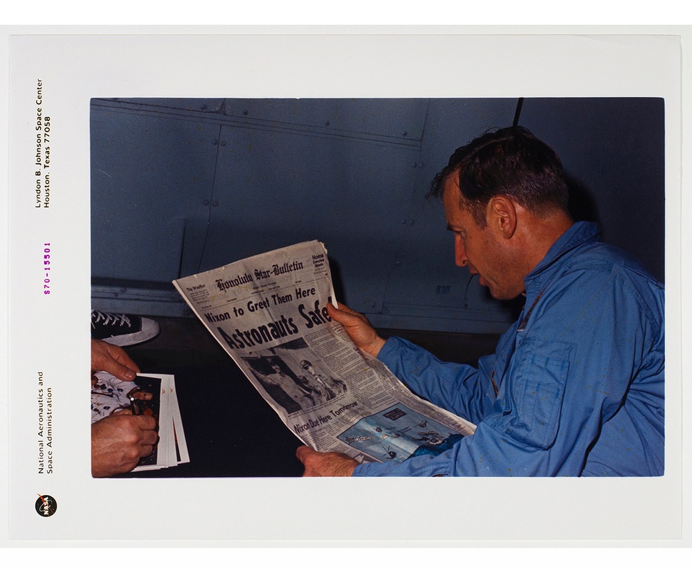 A photograph of a man in a blue shirt who is reading a newspaper headlined “Astronauts Safe!”