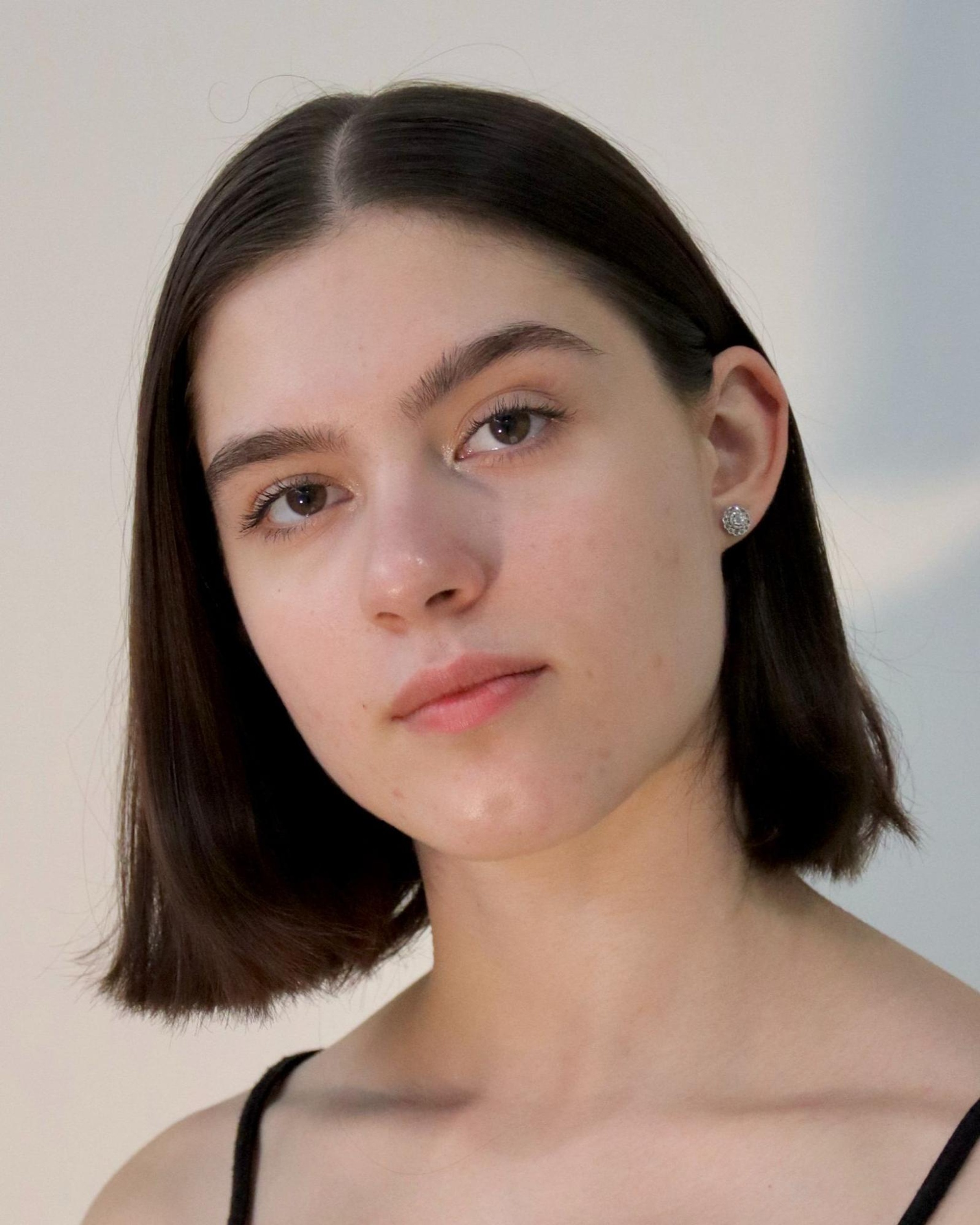 A headshot of dancer Marra Spallone, a white woman with straight brown hair cut just above her shoulders. She looks directly at us, tilting her head with one eyebrow raised. 
