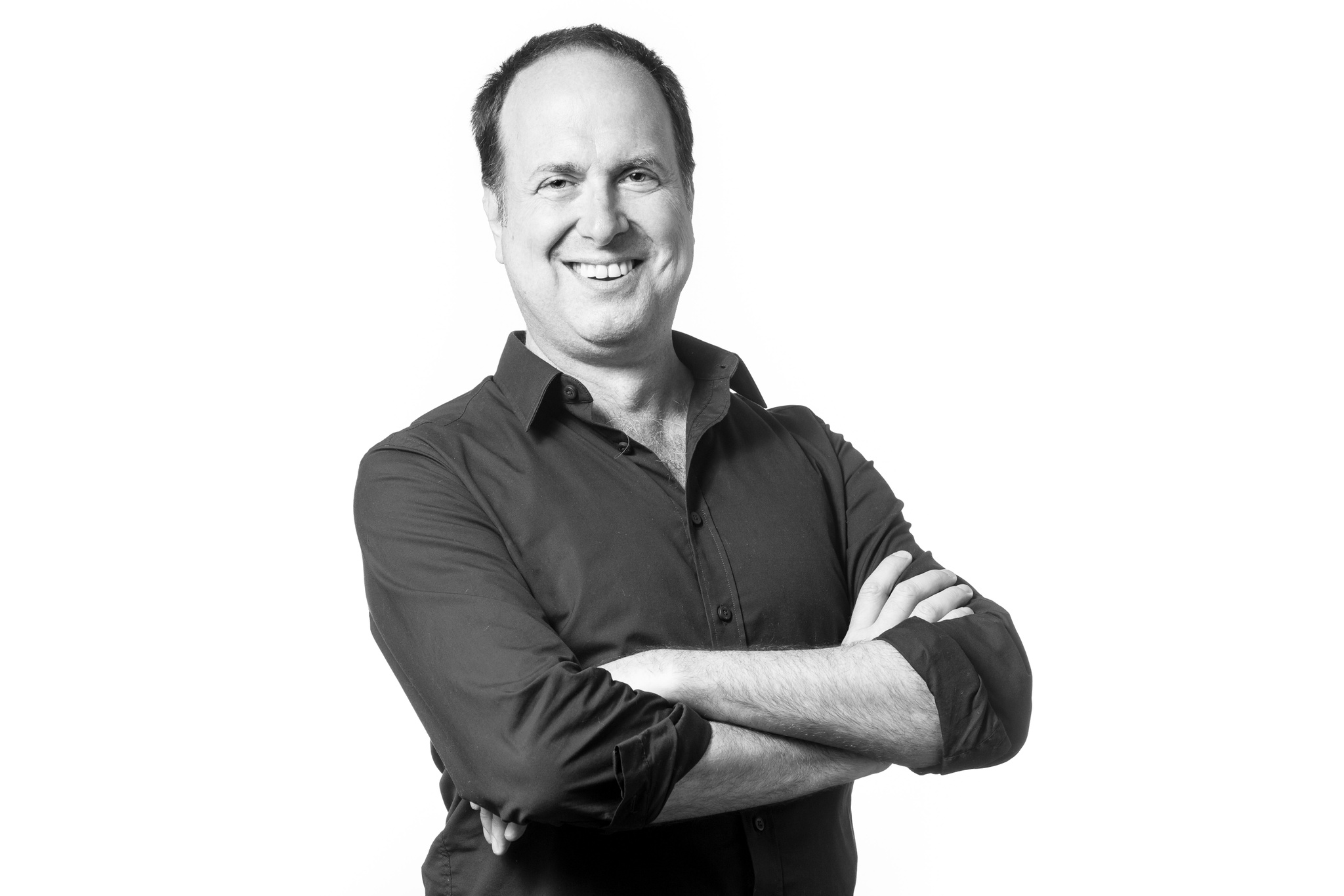 A portrait of Jay Wegman, a white man who poses against a white backdrop with arms crossed over his chest. He smiles and looks at us. 