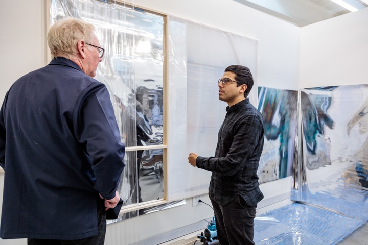 Two people look at a set of artworks hung on the white walls of a private studio space.