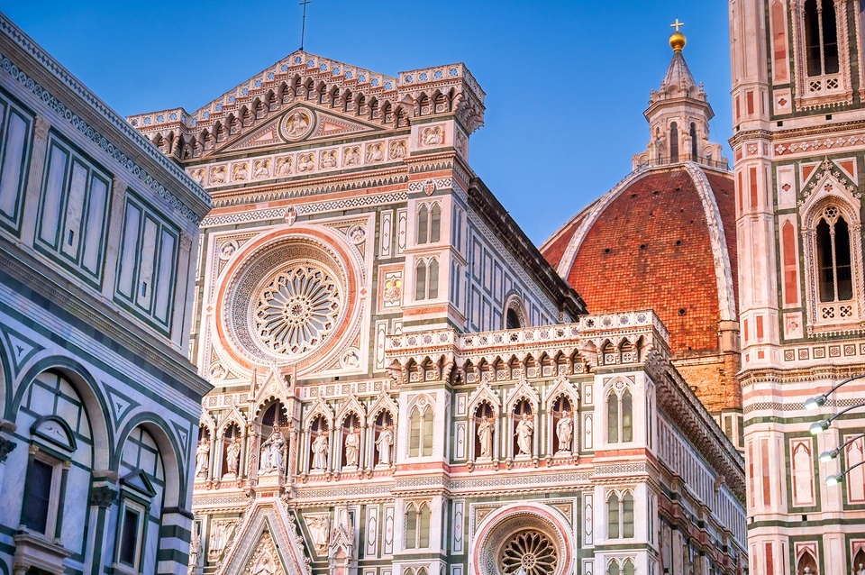 The Santa Maria del Fiore cathedral lit in sunset with a blue sky.