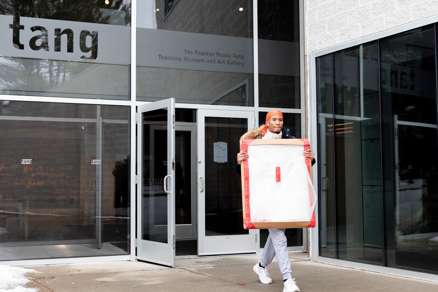 A student is carrying a packaged artwork leaving the Tang.