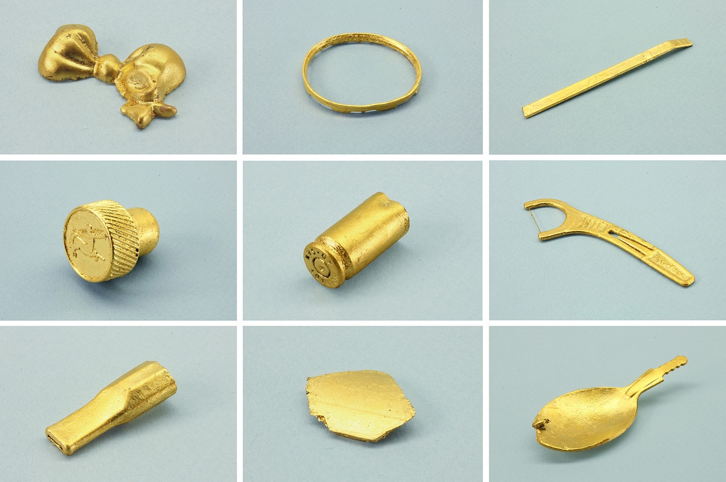 Various gilded/golden objects—including a bracelet, a flat headed screwdriver bit, and a dental flosser, among other things—photographed on a light gray-teal ground.