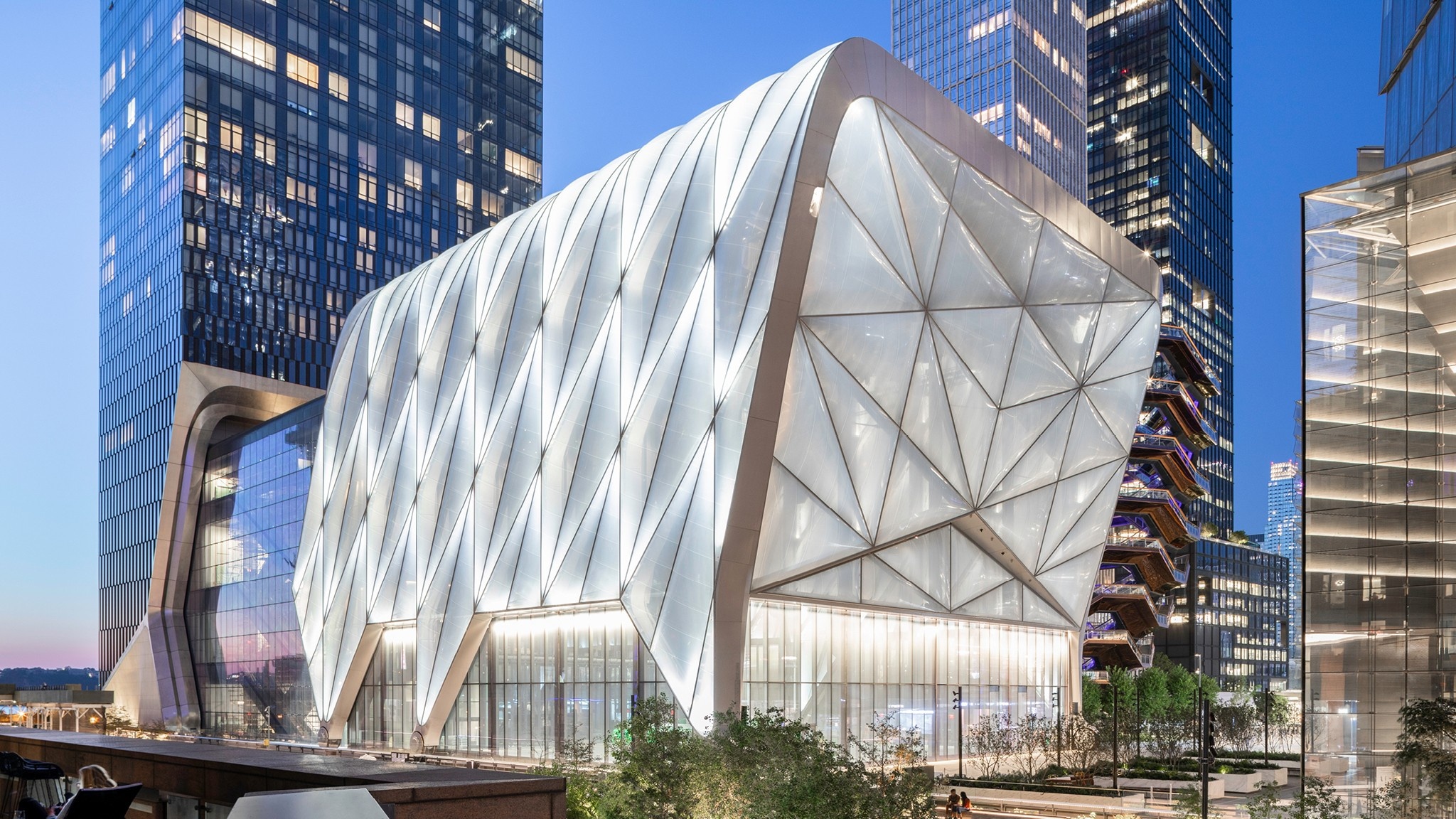 The Shed's south- and east-facing façades at dusk, with the building's movable shell lit and glowing from within