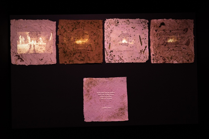 Five sheets of handmade paper inlaid with leaves and wildflowers with verses printed on them. Projected on these sheets are four scenes of fires and one other verse of poetry (illegible).