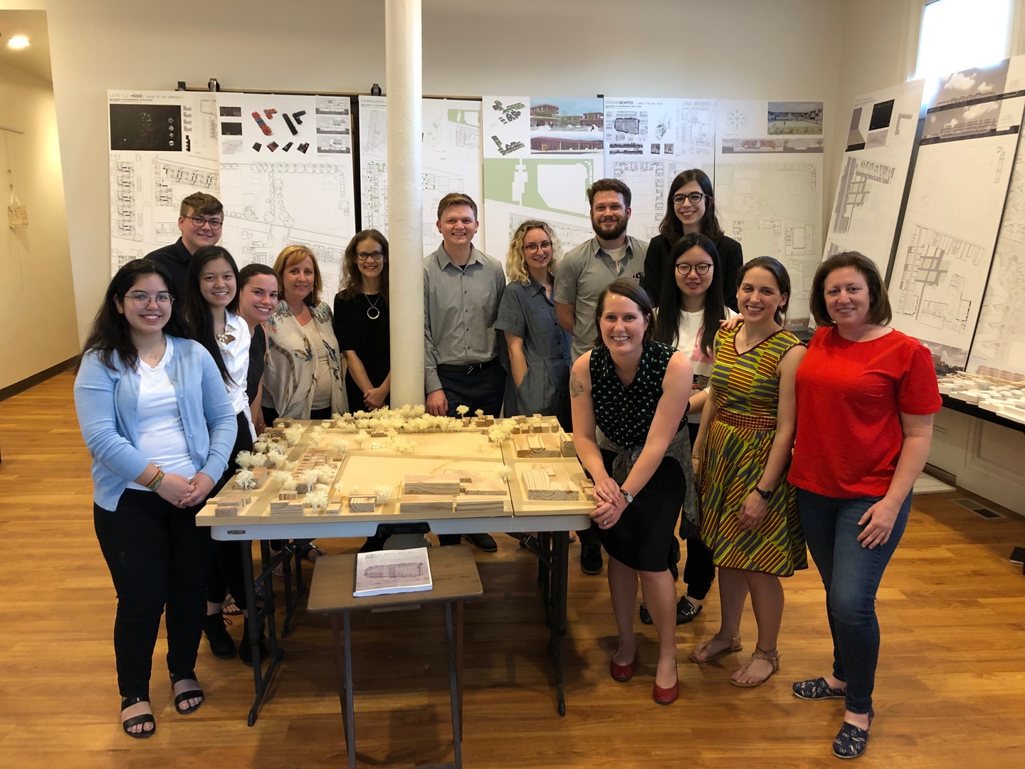 A group of people stand around a model, with boards of architectural work surrounding them.