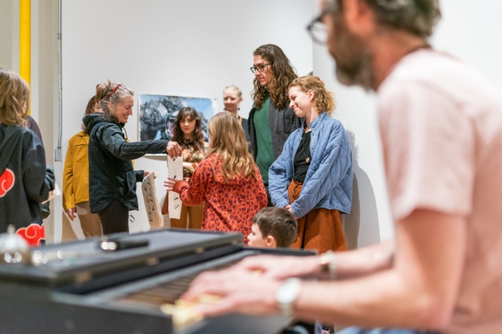 Performance piece with one student on keyboard while another hands out strips of fabric with poetry imprinted on them to gallery attendees at a show.