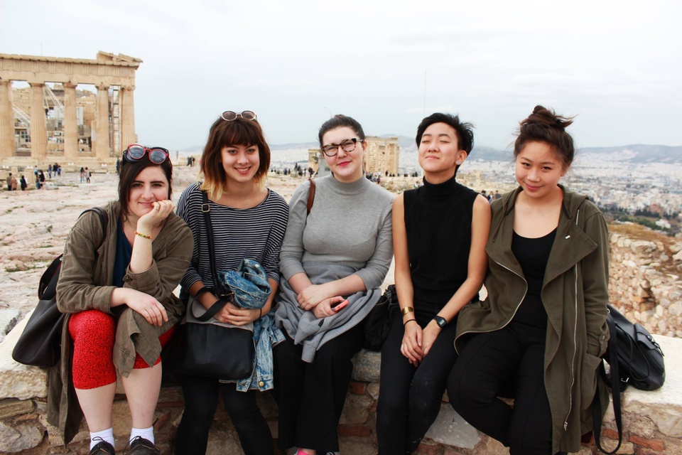 Four people sitting on a low wall in front of the acropolis in Athens, Greece.